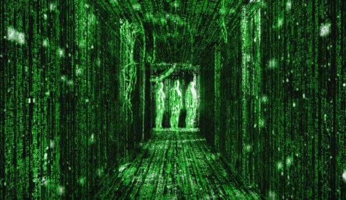 Un fotograma de la película Matrix. Se ve un pasillo de unos 5 o 6 metros de largo y uno y medio de ancho, con varios huecos de puertas a lo largo de las paredes, unos cables colgando desde el techo y tres hombres vestidos de traje al fondo. Es una imagen generada por ordenador que representa la comprensión de Neo del mundo virtual de Matrix, así que todo en la imagen está formado por trazas de texto en color verde fósforo que recorren cada superficie.