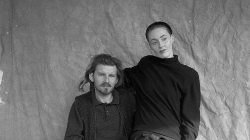 Fotografía en blanco y negro de Brendan Perry y Lisa Lisa Gerrard, los componentes de Dead Can Dance. Él está sentado en una silla (fuera de plano) y lleva un polo con un chaleco estampado por encima, con barba poco poblada y bigote más marcado, así como el pelo negro, mientras mira a cámara. Ella parece estar sentada sobre él, pasándole un brazo por encima del hombro, mientras mira hacia el lado; lleva el pelo recogido bajo un gorro ceñido y viste un jersey.