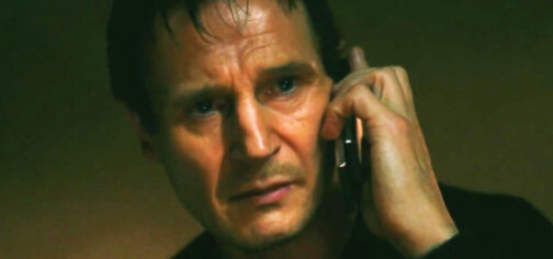 Primer plano de Liam Neeson, mirando hacia nosotros, con cara de concentración mientras escucha lo que le dice alguien por teléfono antes de que él mismo le conteste que no le va a hacer caso y que no sabe con quién se están metiendo. la imagen tiene un fondo oscuro de color marrón verdoso y la iluminación es muy contrastada, acentuando el dramatismo. Es un fotograma de la película Venganza (Taken), una saga plagada de argumentos tópicos y bandera del cine de tipos duros en los últimos años.