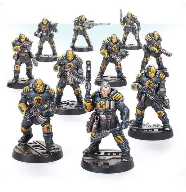 Fotografía de una patrulla de Palatine Enforcers. Se trata de 10 miniaturas con uniforme de combate y placas de armadura en pectural, hombros, brazales y grebas, en color azul-gris oscuro con decoraciones en amarillo anaranjado. Van equipados con granadas cilíndricas, pistolas, escopetas de combate y bolters de aspecto bastante amenazador.