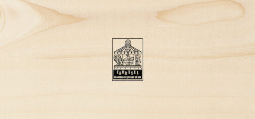 Sobre una textura de madera clara y porosa, el logo del Carrusel Bloguero de Juegos de Rol. Es un rectángulo vertical con un tiovivo de feria coronado por un dado de 20 caras, cuyas monturas son una imagen de Cthulhu, un caballero armado a caballo y una armadura de combate tecnológica. Bajo el tiovivo aparecen las letras grandes CARRUSEL ondulando arriba y abajo, y bajo esas, ocupando el mismo ancho, BLOGUERO DE JUEGOS DE ROL.
