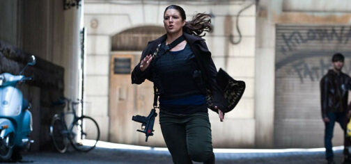 Mallory Kane, la dura protagonista de la película Indomable (Haywire) de Steven Soderbergh, corriendo por un callejón con su abrigo abierto al viento que deja a la vista un chaleco táctico, una pistola en pistolera sobaquera y un subfusil colgando de su hombro derecho. Tiene expresión de esfuerzo pero de quedarle fuerzas de sobra para reventar a puñetazos a Ewan McGregor sin despeinarse.