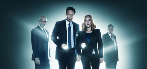 Fotografía promocional de Expediente X (X-Files) mostrando a Mulder y Scully en primer plano, mirando a cámara mientras la enfocan con linternas de mano. Ellos dos están como rodeados de un halo de luz como si tuvieran un foco detrás y a medias de cubrir por esa misma luz aparecen por detrás las figuras de Skinner y el Fumador.