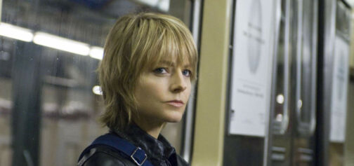 Primer plano de Erica Bain, la protagonista de La extraña que hay en mí (The Brave One) sentada en un vagón de metro frente a una de las ventanas. Es la actriz Jodie Foster, con el pelo cortado a la altura del cuello, flequillo largo que le cae sobre los ojos, con una cazadora de piel negra y la cinta azul de un bolso sobre el hombro.