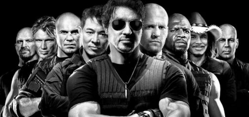 Imagen de un cuarto (busto) de The Expendables, en su formación original, en blanco y negro, encabezados por Silvester Stallone, con gafas, y detrás de él, de izquierda a derecha: Steve Austin, Dolph Lundgren, Randy Couture, Jet Li, Jason Statham, Terry Crews, Mickey Rourke y Bruce Willis.