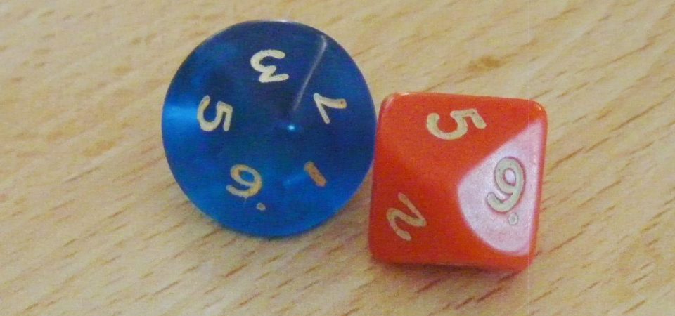 Los 2d10 originales con los que empezó todo. El génesis del frikismo. Es una fotografía de mala calidad de un primer plano de ambos dados sobre un tablero de madera clara. El de la izquierda es azul oscuro, traslúcido, con letras blancas, mostrándose casi "de punta" hacia la cámara de forma que se ve prácticamente circular mientras muestra sólo las caras de los resultados impares con un resultado de 3. El de la derecha es naranja butano con letras blancas y está en una posición más de lado, un poco en la forma que se suele representar icónicamente el d10, mostrando el resultado de 5 y otras dos caras legibles con el 9 y el 2.