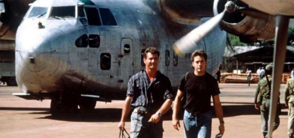 Dos hombres; uno de mediana edad vestido con camisa de cuadros azules y pantalones cargo, el otro con camiseta negra y vaqueros azules, caminan alejándose de un avión bimotor de hélices de aspecto viejo y sucio. Es un fotograma de la película Air America, sobre contrabandistas de la CIA. Algo que podría llevarse a cabo con Savage Worlds para Tipos Duros.