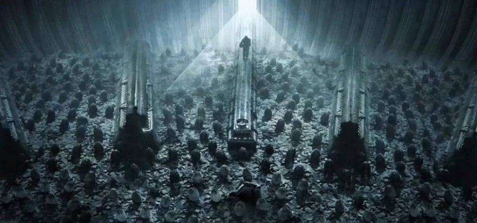 Vista contrapicado de una especie de almacén de huevos de aliens, seguramente un fotograma de una de las últimas películas de la saga, en tonos grises azulados. El suelo está plagado de huevos y de una puerta en la parte superior de la imagen, y de la que surge una luz muy potente, entra un ser humanoide.