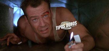 Imagen de La jungla de Cristal, con John McLane arrastrándose por los conductos de ventilación mientras se ilumina con un mechero de tipo zippo. Es un hombre de unos 40 años, con los ojos azules, el pelo corto con abundantes entradas y una camiseta interior blanca de tirantes. Está cubierto de mugre y salpicaduras de sangre. Por encima, a un lado de la cara de John está sobreimpreso el logo de Tipos Duros, el juego de rol: el texto Tipos Duros en letras blancas grandes y cuadradas, con una inclinación de unos 15º hacia la derecha y debajo, letra más pequeña pero con las mismas características Edición Aventura, todo girado unos 15º a contrarreloj y superpuesto al logo de Savage Worlds Fans Product.