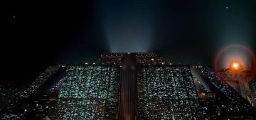 Icónico fotograma de Blade Runner mostrando durante la noche la arcología de Tyrell Corporation, en su descomunal masa de cientos de metros de alta y miles de ventanas iluminadas, mientras un coche volador se acerca a ella.
