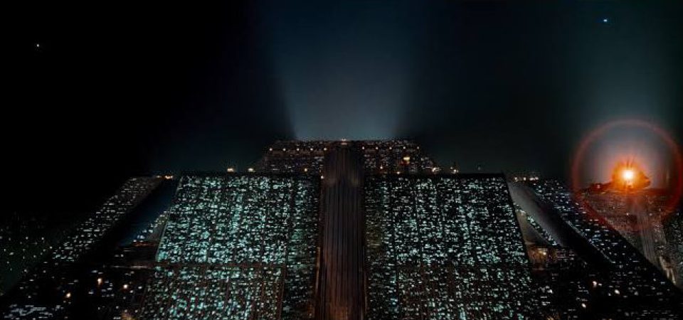 Icónico fotograma de Blade Runner mostrando durante la noche la arcología de Tyrell Corporation, en su descomunal masa de cientos de metros de alta y miles de ventanas iluminadas, mientras un coche volador se acerca a ella.