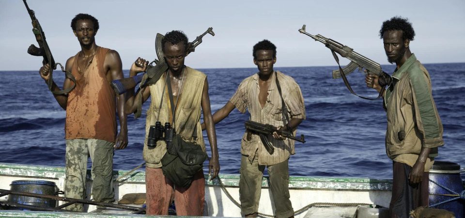 Cuatro piratas del mundo moderno de la película Capitán Phillips. Son cuatro personas negras, con ropas muy sucias y estropeadas, el pelo cortado de manera irregular y empuñando fusiles de asalto AK-47, mientras se encuentran de pie en una lancha de color verde irregular y llena de bidones de, cabos y diferentes aparejos. El ejemplo de lo que representan los piratas para Savage Worlds de Tipos Duros.