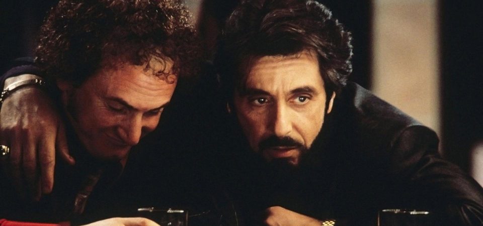 Fotograma de la película Carlito's Way (Atrapado por su pasado), con un primer plano del personaje de Al Pacino pasando el brazo por encima de los hombros a otro mientras se apoyan en la barra de un bar en la que se ven algunos vasos. Ambos llevan ropa oscura y la imagen tiene una iluminación escasa para que toda la atención se vaya a los rostros. Una película clave para entender lo que es un Oscuro Pasado.