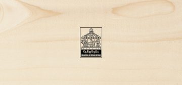 Sobre una textura de madera clara y porosa, el logo del Carrusel Bloguero de Juegos de Rol. Es un rectángulo vertical con un tiovivo de feria coronado por un dado de 20 caras, cuyas monturas son una imagen de Cthulhu, un caballero armado a caballo y una armadura de combate tecnológica. Bajo el tiovivo aparecen las letras grandes CARRUSEL ondulando arriba y abajo, y bajo esas, ocupando el mismo ancho, BLOGUERO DE JUEGOS DE ROL.
