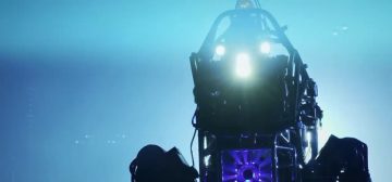 En un fondo saturado de diferentes fuentes de luz azul se recorta la estructura de tubos metálicos, ventilación iluminada en morado y los tres focos de luz de un robot de DARPA, dándole un aspecto un poco de película de terror.
