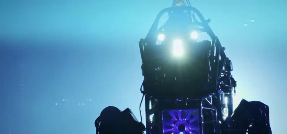 En un fondo saturado de diferentes fuentes de luz azul se recorta la estructura de tubos metálicos, ventilación iluminada en morado y los tres focos de luz de un robot de DARPA, dándole un aspecto un poco de película de terror.