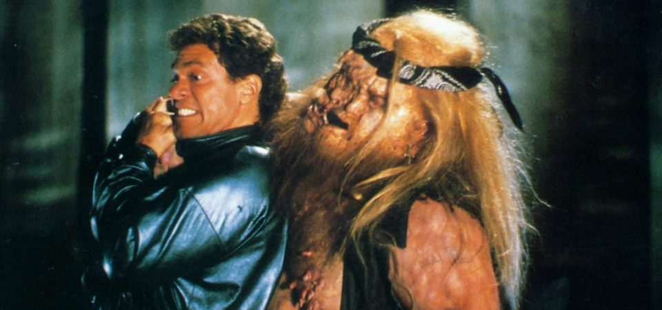 El zombie deforme de un pandillero al que parece que la cara se le está desdoblando y que tiene decenas de pezones ataca a un tipo con el pelo rizado y una chaqueta de piel absolutamente ochentera. Es un fotograma de la película Dead Heat, que en España se llamó Estamos muertos... ¿o qué?