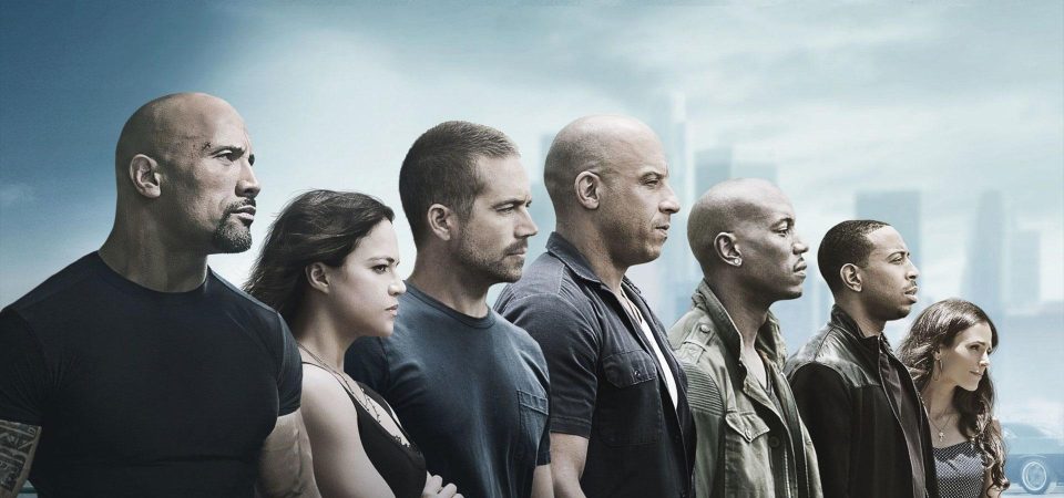 Varios personajes de la saga Fast & Furious, en vista lateral hacia la derecha, sobre un paisaje azul gris de humo en el que se adivina el skyline difuso de una gran ciudad. De izquierda a derecha, superponiéndose uno a otro, se encuentran Luke Hobbs (Dwayne Johnson), Letty Ortiz (Michelle Rodriguez), Brian O'Conner (Paul Walker), Dom Toretto (Vin Diesel, ocupando justo el centro de la imagen), Rome Pearce (Tyrese Gibson), Tej Parker (Ludacris) y Mia Toretto (Jordana Brewster). A lo largo de las películas son un ejemplo de personajes que subliman y cambian sus Ideales debido a como cambian sus circunstancias vitales.