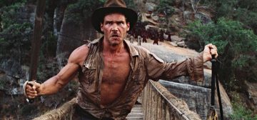 Fotograma de Indiana Jones y el templo maldito. Indiana Jones, con la camisa desgarrada abierta por el pecho y a la que le falta todo un brazo, se encuentra en un puente de cuerda sosteniendo una bolsa en la mano izquierda y un sable en la mano derecha, amenazando con lanzar la bolsa al suelo si sus enemigos se acercan. Sí, lleva su sombrero fedora. El escenario es una agreste montaña de riscos resquebrajados entre cuyas grietas crece una frondosa vegetación. Jones es un ejemplo de características tan marcadas que pueden utilizarse para dar carácter a los PNJs.