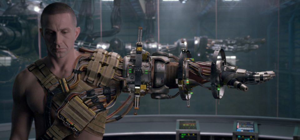 Forograma de la película Pacific Rim en la que se ve a un hombre, desnudo de cintura para arriba y con el pelo rapado, con el brazo izquierdo extendido por completo. Lleva un arnés lleno de cables, sensores y baterías que se extiende a lo largo de varios soportes y articulaciones alrededor del brazo.