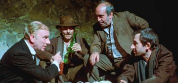 Fotograma de la película Parranda (1977), donde en primer plano Fernando Fernán-Gómez, a la izquierda y vestido de negro, José Sacristán, a la derecha vestido de marrón, y, detrás a la izquierda, José Luís Gómez de marrón y con sombrero mientras sostiene una botella de vino de casco verde, atiende junto a Fernando Ferrandis, detrás a la derecha en gris y verde, atendiendo a lo que habla Fernán-Gómez.