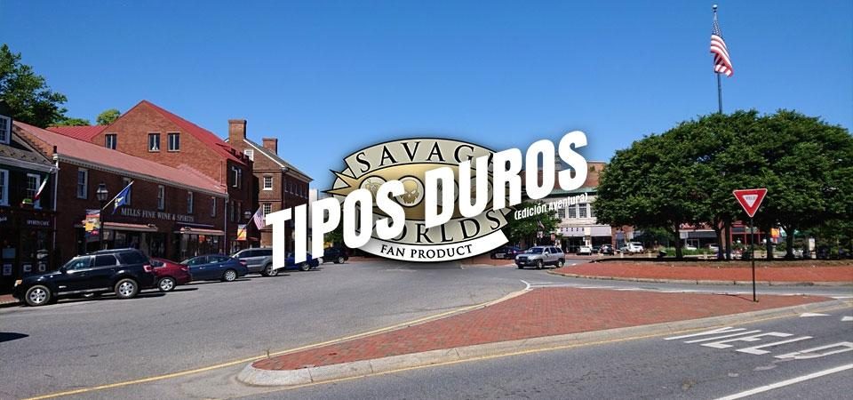 Una calle cualquiera de una zona residencial de una ciudad de estados unidos. Podría ser perfectamente de Wildspring, la ciudad que da nombre a la serie homónima. Alrededor de un cruce de amplias calzadas, edificios de uno o dos pisos, de ladrillo rojo visto y abundantes coches circulando o aparcando. Hay una rotonda central cubierta de árboles entre los que sobresale el mástil de una bandera de los Estados Unidos. Sobre la imagen está impreso el logo de Tipos Duros, el juego de rol: el texto Tipos Duros en letras blancas grandes y cuadradas, con una inclinación de unos 15º hacia la derecha y debajo, letra más pequeña pero con las mismas características Edición Aventura, todo girado unos 15º a contrarreloj y superpuesto al logo de Savage Worlds Fans Product.