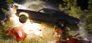 Fotograma de la película Death Proof, en una escena nocturna. Un coche deportivo clásico negro, del tipo muscle car, arrolla a toda velocidad el habitáculo de otro coche, de color rojo, arrancando el techo en medio de una explosión y saltando por los aires. Algo habitual en la serie Wildspring y su adaptación al juego de rol Tipos Duros, para Savage Worlds.