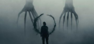 Fotograma de la película La Llamada (Arrival). En un ambiente nebuloso se ve la figura de una mujer de espaldas, frente a un símbolo circular que parece escrito con tinta y vapor, mientras más allá se recortan contra el fondo claro las figuras de dos entidades extraterrestres de aspecto de cefalópodos de patas articuladas. Un ejemplo de cine donde el lenguaje en el worldbuilding se convierte en el eje central del argumento. Un ejemplo un tanto extremo que no suele ocurrir en literatura o juegos de rol.