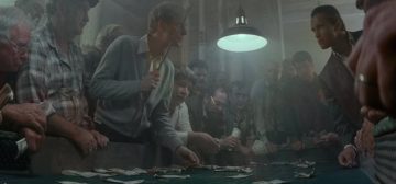 Fotografía de una mesa de juego ilegal, con docenas atde hombres de todo aspecto y procedencia que atestan sus bordes, apostando con billetes gastados bajo la luz de una única lámpara en un ambiente cargado del humo del tabaco. Un clásico de los negocios de las organizaciones criminales.