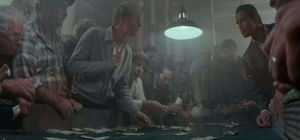 Fotografía de una mesa de juego ilegal, con docenas atde hombres de todo aspecto y procedencia que atestan sus bordes, apostando con billetes gastados bajo la luz de una única lámpara en un ambiente cargado del humo del tabaco. Un clásico de los negocios de las organizaciones criminales.