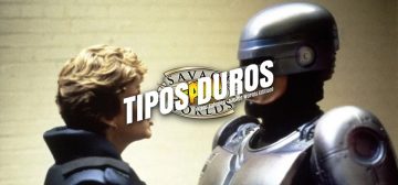 Un fotograma de Robocop de 1987, en que la agente Lewis y Robocop están mirándose de cara mientras hablan. Lewis es una mujer rubia con el pelo corto y un pendiente dorado de aro en la oreja, vestida con el uniforme azul del departamento de policía de Detroit. Robocop es un cyborg, con todo el cuerpo, incluyendo la mayor parte de la cabeza, cubierto por una coraza metálica de color acero azulado; sólo le queda visible como orgánico la parte del rostro que comprende los carrillos y los labios. Encima del fotograma el logo de Tipos Duros: el texto Tipos Duros en letras blancas grandes y cuadradas, con una inclinación de unos 15º hacia la derecha y debajo, letra más pequeña pero con las mismas características "Tipos Salvajes - Savage World Edition", todo girado unos 15º a contrarreloj y superpuesto al logo de Savage Worlds Fans.