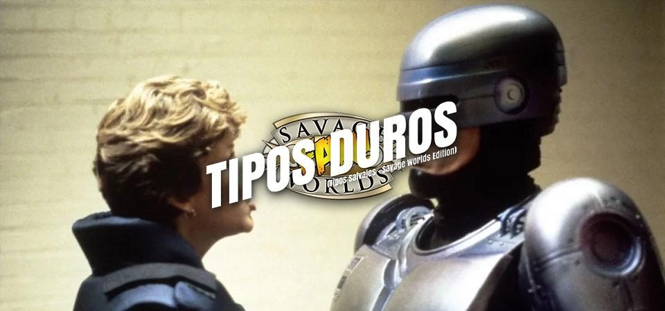 Un fotograma de Robocop de 1987, en que la agente Lewis y Robocop están mirándose de cara mientras hablan. Lewis es una mujer rubia con el pelo corto y un pendiente dorado de aro en la oreja, vestida con el uniforme azul del departamento de policía de Detroit. Robocop es un cyborg, con todo el cuerpo, incluyendo la mayor parte de la cabeza, cubierto por una coraza metálica de color acero azulado; sólo le queda visible como orgánico la parte del rostro que comprende los carrillos y los labios. Encima del fotograma el logo de Tipos Duros: el texto Tipos Duros en letras blancas grandes y cuadradas, con una inclinación de unos 15º hacia la derecha y debajo, letra más pequeña pero con las mismas características "Tipos Salvajes - Savage World Edition", todo girado unos 15º a contrarreloj y superpuesto al logo de Savage Worlds Fans.